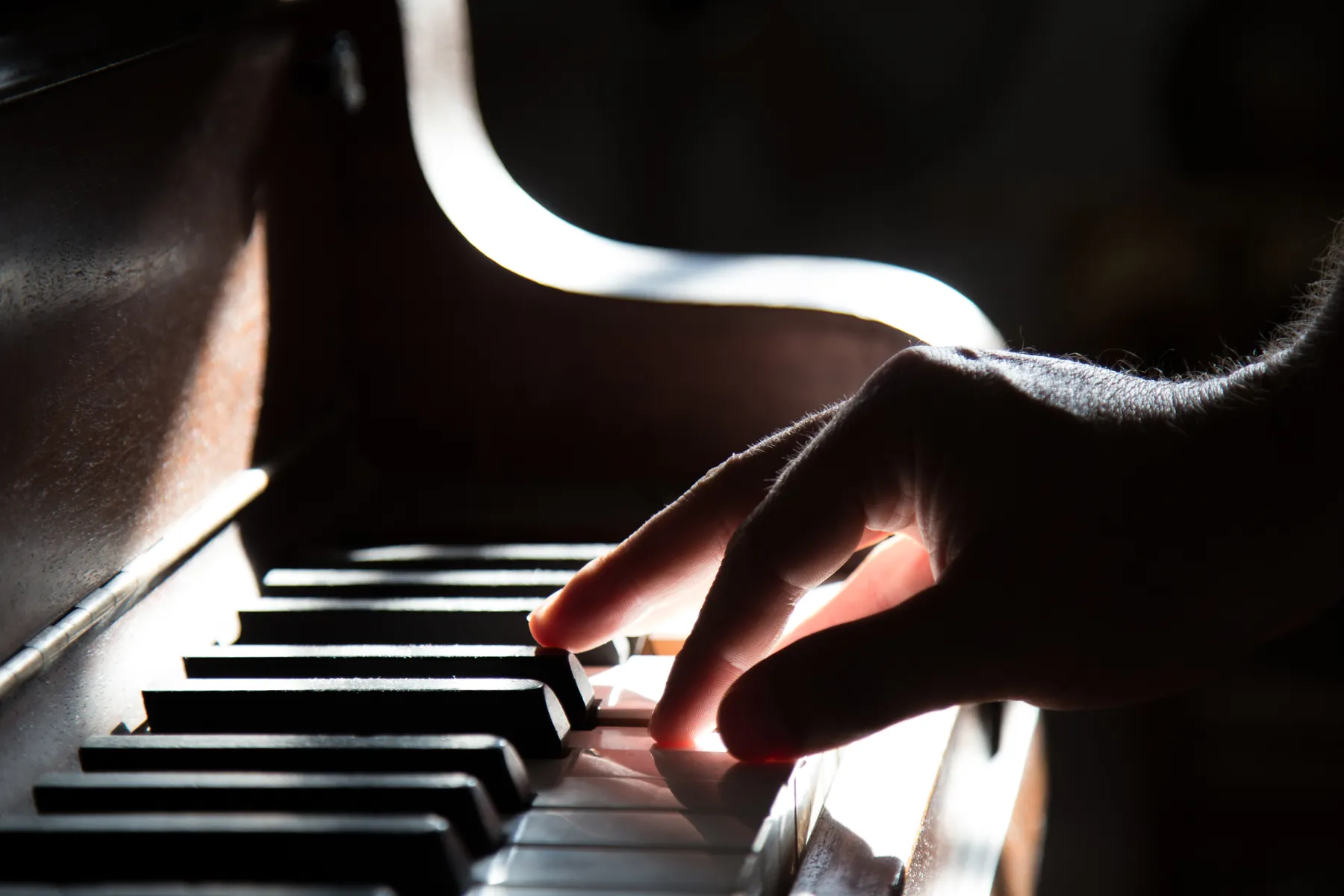 Nahaufnahme: Eine Hand spielt im warmen Gegenlicht auf den Tasten eines Klaviers