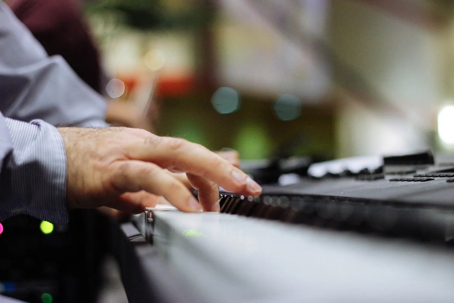 Die Hand eines älteren Mannes spielt auf einem Keyboard, im Hintergrund unscharfes warmes Licht